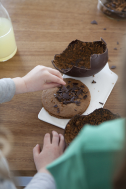 œuf Dandoy au chocolat fondant en morceaux et à la poudre de speculoos et mains de petite fille effritant des bouts de chocolat