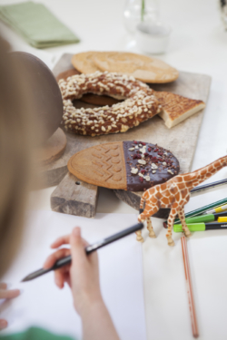 petite fille qui colorie sur une table sur laquelle on voit un œuf speculoos au chocolat fondant et un pain à la grecque
